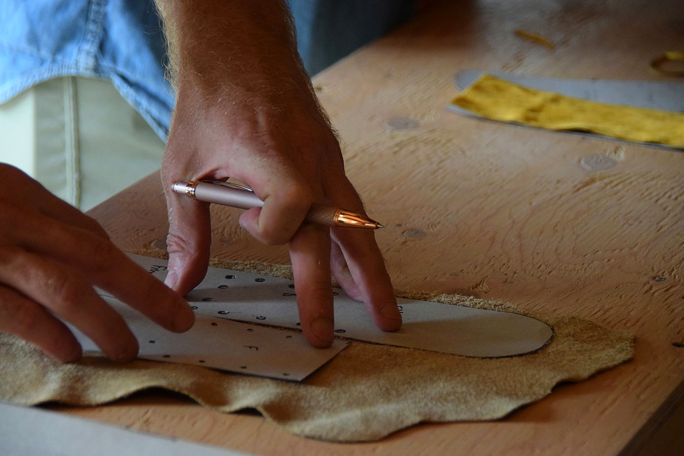 Hands marking a leather pattern by hand before cutting